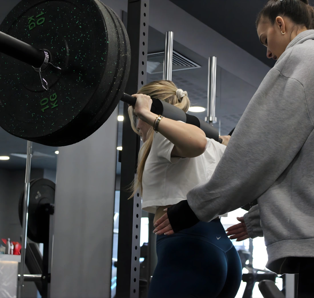 Coach του ForeverFit καθοδηγεί ασκούμενη σε άσκηση με μπάρα